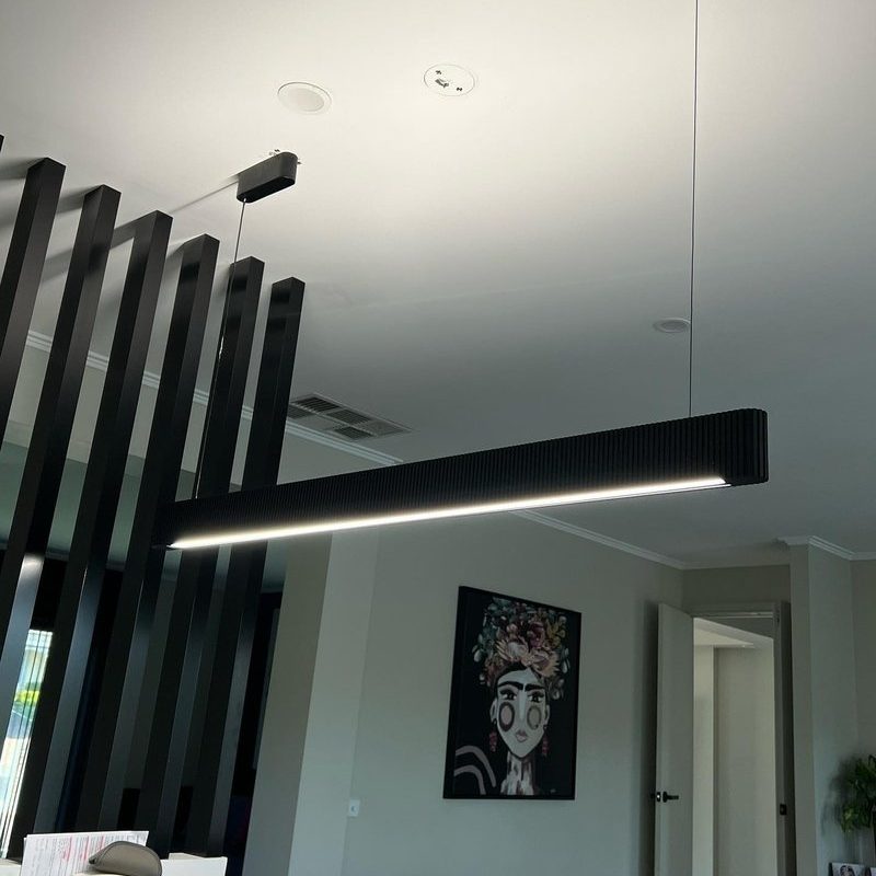 Black linear LED pendant light beside a divider of black battens