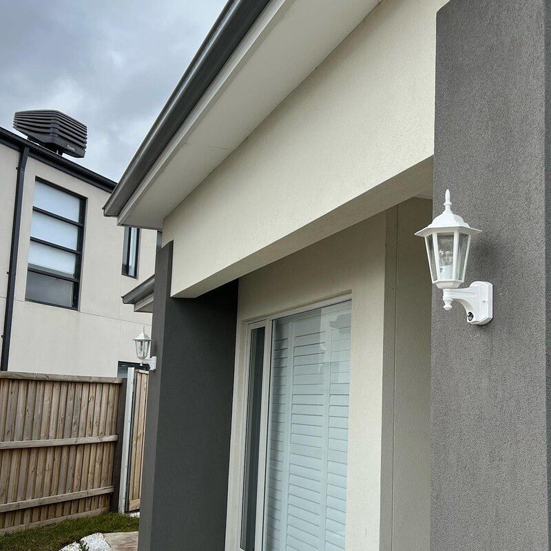 White coach-style outdoor wall light on a rendered house wall