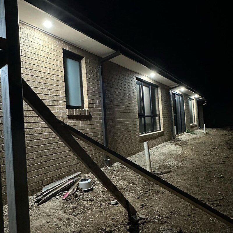 New brick home at night with eave downlights over a dirt yard