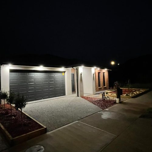 Single-storey house and front garden lit at night by eave downlights