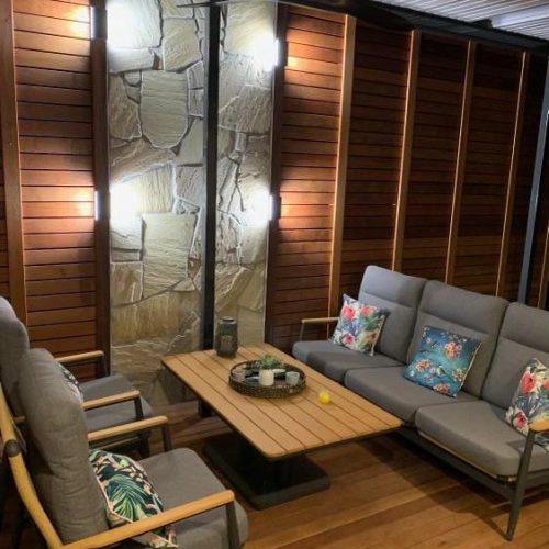 Covered outdoor lounge with stone feature wall lit by wall lights